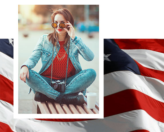 a seated women with sunglasses in a red shirt, blue jeans, and a denim jacket